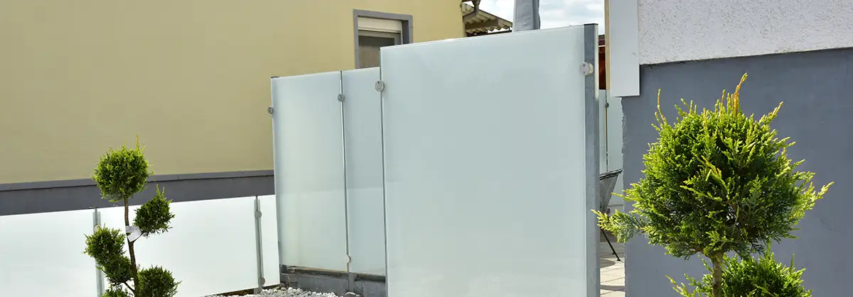 Terrasse und Gartenbereich mit Ziergehölz und Schotterbeet hinter einem Wohnhaus mit Milchglas-Sichtschutz um den Essbereich