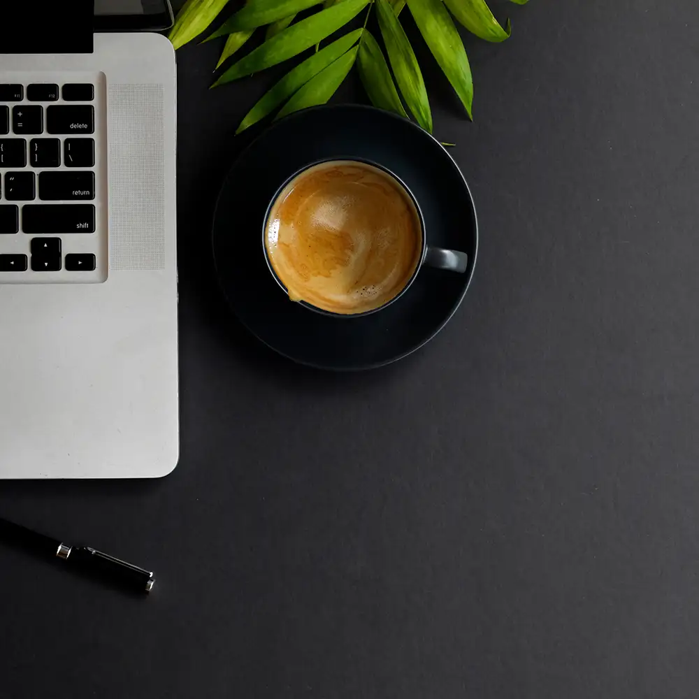 dark workspace mit schwarzer Kaffeetasse, Laptop und Pflanze auf dunklem Tisch.